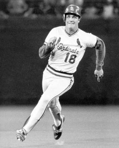 black and white image of man in major league baseball uniform and batting helmet running around bases.