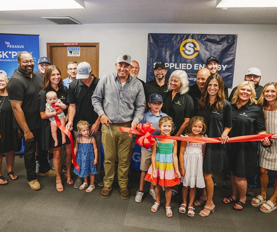A group of smiling people, including adults and children, gather for a ribbon-cutting ceremony. The mood is celebratory, with a backdrop of banners.