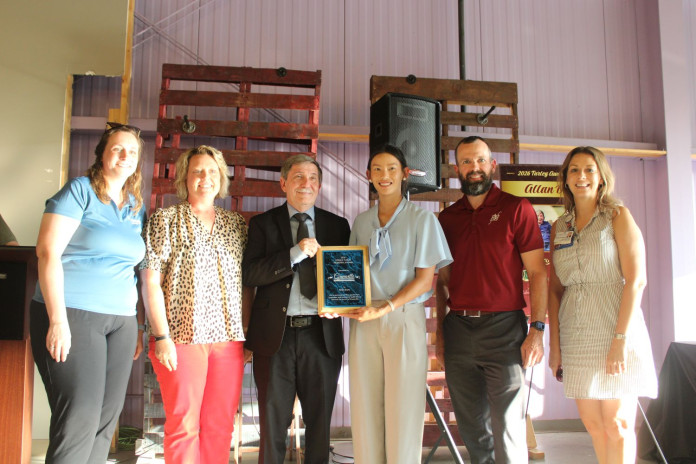 A diverse group of individuals stands united, showcasing an award while expressing happiness and achievement.
