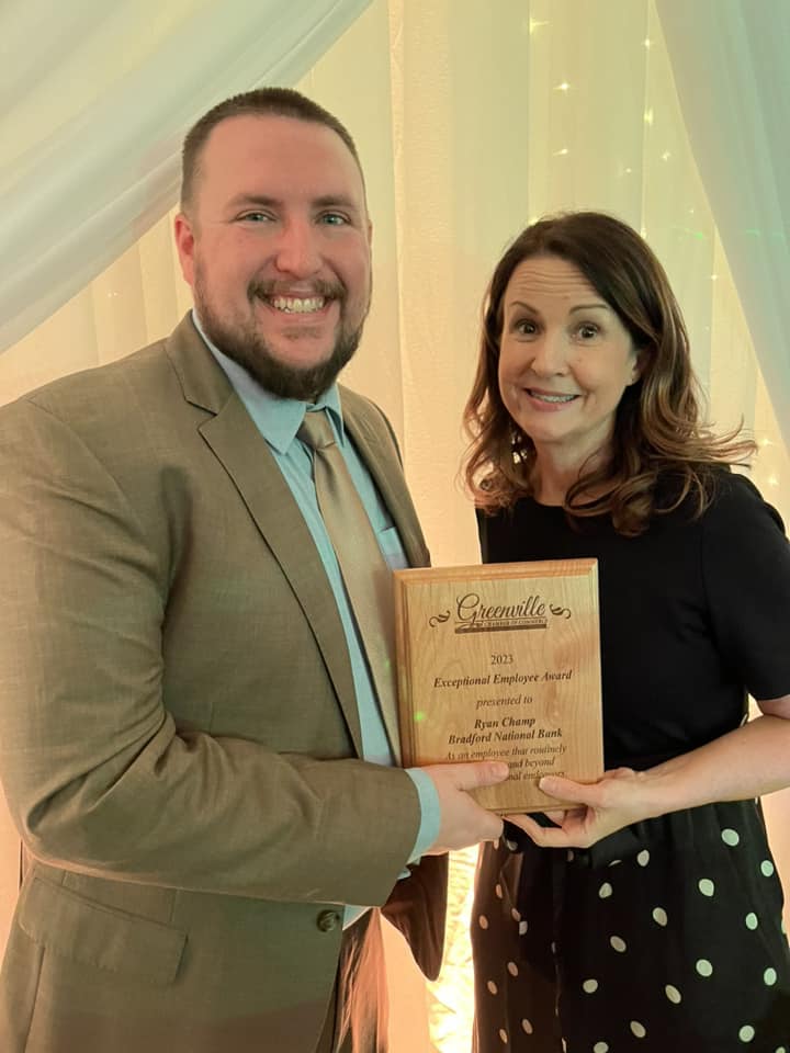 man in brown jacket and tie and woman in black cocktail dress hold wooden award plaque