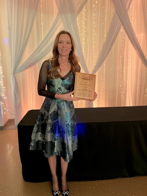 woman in green and black coctail dress holds wooden award plaque